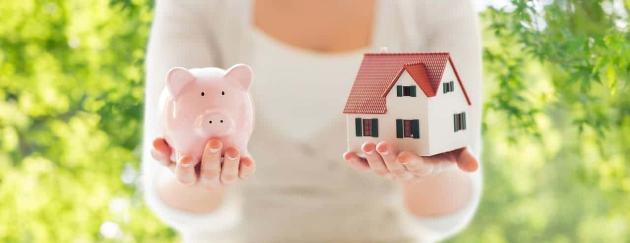 Manos sosteniendo hucha cerdo y modelo casa